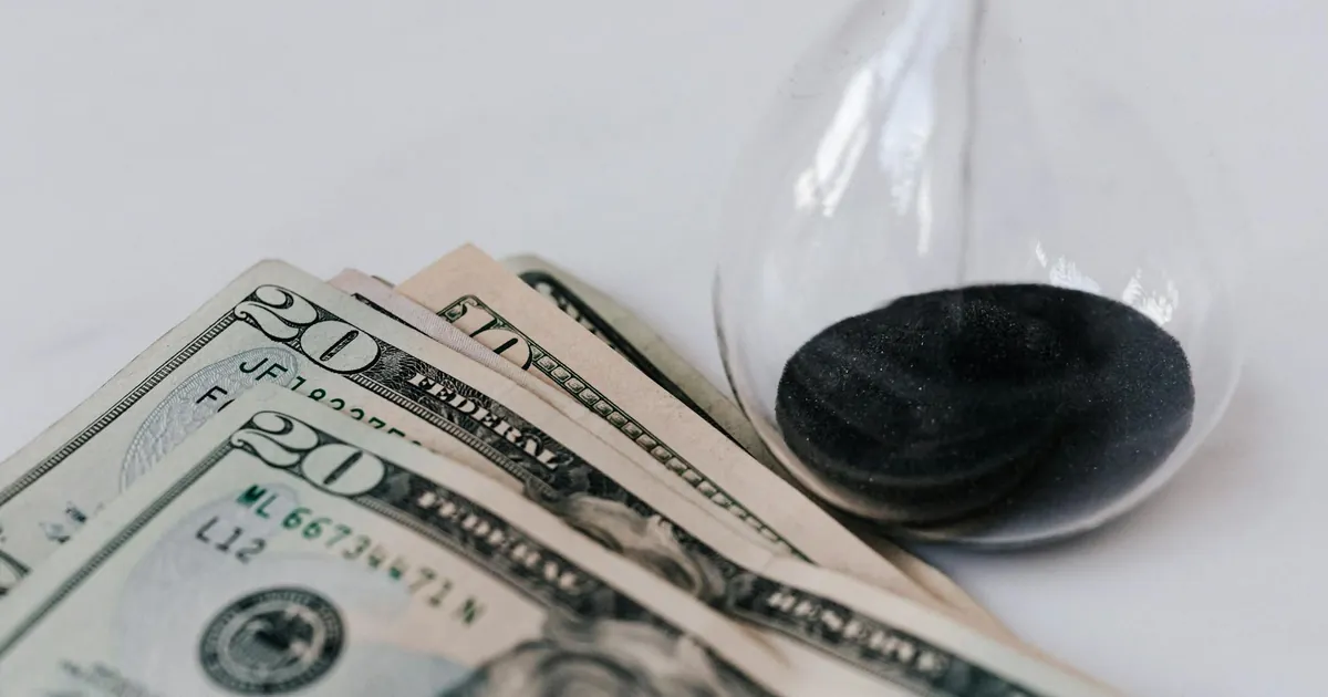 From above transparent hourglass with flares on fragile surface near pile of banknotes with numbers and official seal