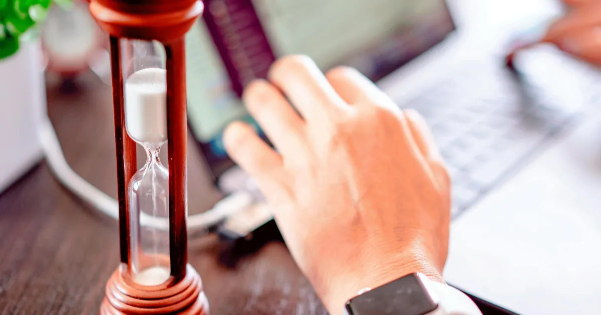 Close-up of a hand on a laptop with an hourglass, symbolizing time management and productivity.