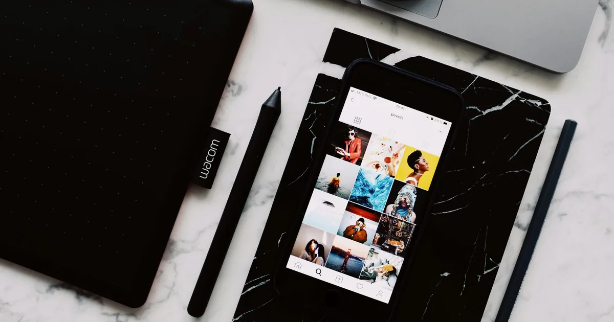 From above of marble table with black textbook and cellphone above with opened app showing interesting photo gallery on screen